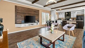 A modern living room with a flat-screen TV, a coffee table, and a dining area with chairs. - 8 acres Ranch - 3 Homes - Sleeps 24 - Dripping (Dripping Springs)