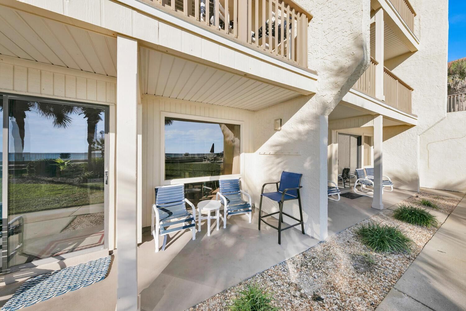 A modern building with a spiral staircase, outdoor seating area with chairs, and large windows offering views of the ocean.