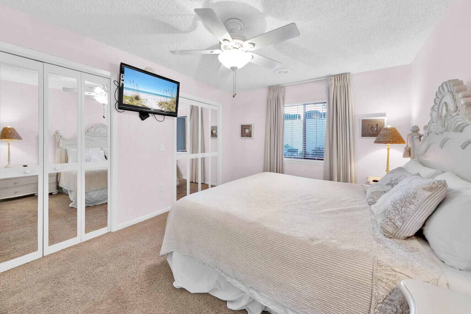 A bedroom with a bed, a ceiling fan, a TV, and a window with curtains.