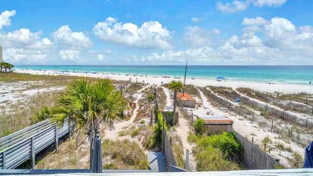 Ein Strand mit blauem Himmel, sandigem Ufer und einigen Gebäuden in der Ferne.