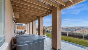 En overdækket terrasse med jacuzzi, udendørs møbler og udsigt over det omkringliggende landskab.