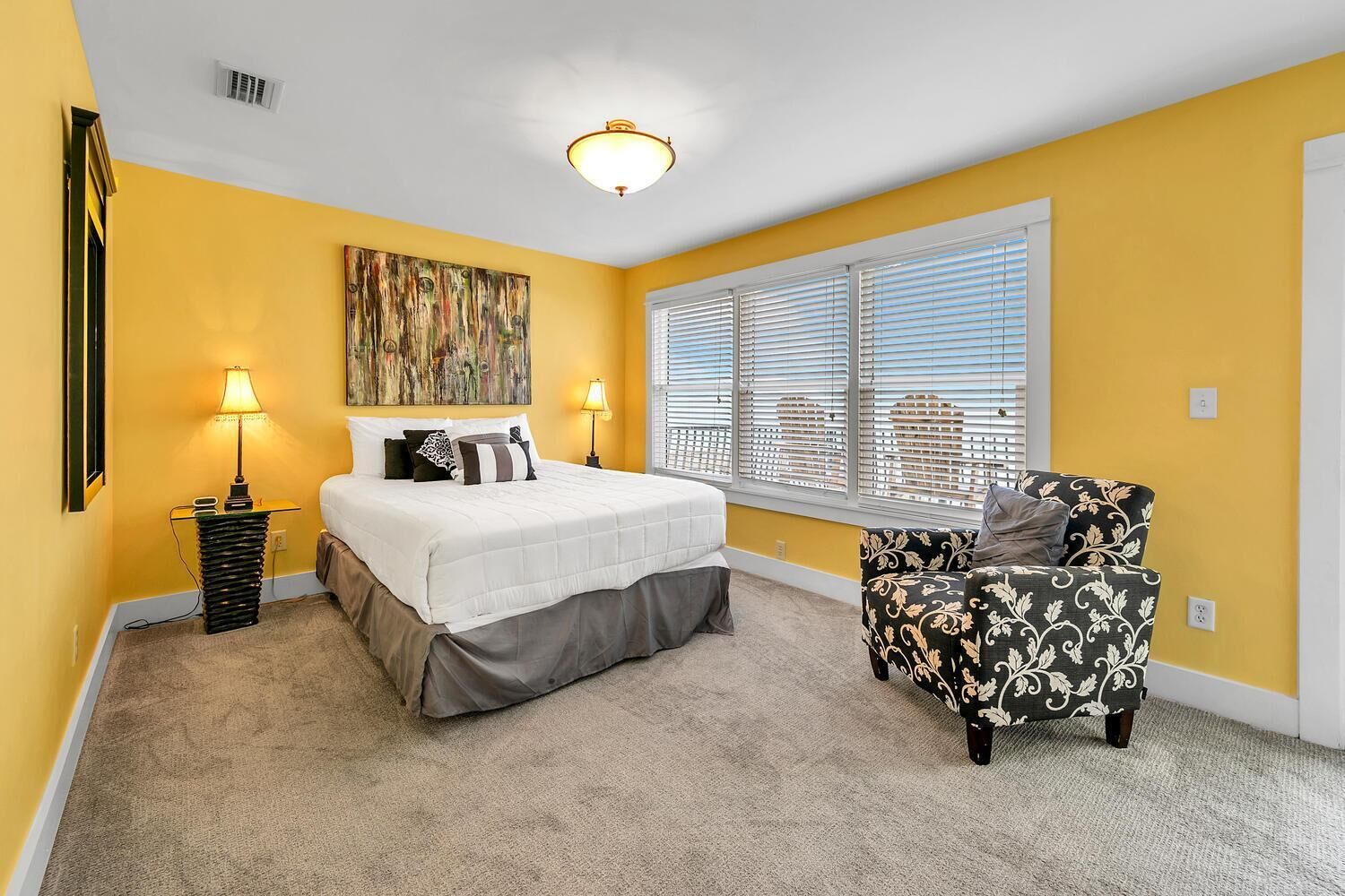 A bedroom with a bed, two bedside lamps, a chair, a window with blinds, and a ceiling light.