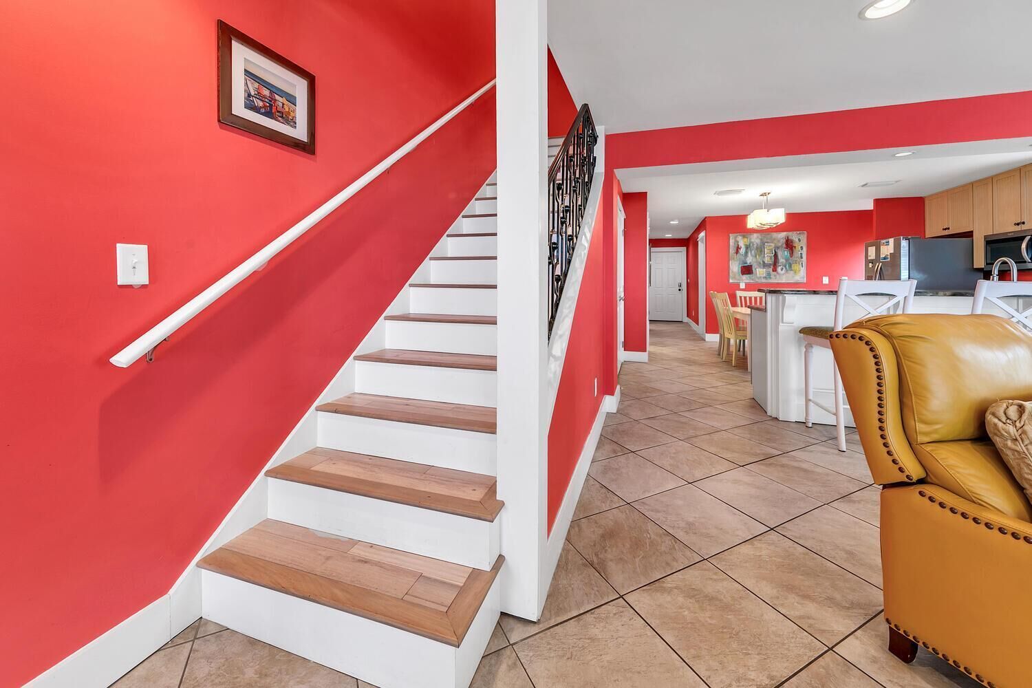Una escalera con escalones de madera y paredes blancas que conduce a una zona de cocina con una mesa y sillas.