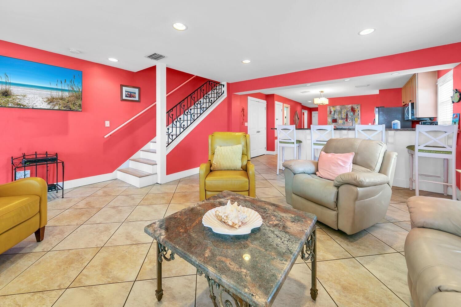 A spacious living room with a red accent wall, a staircase, and a kitchen area visible through an open doorway.