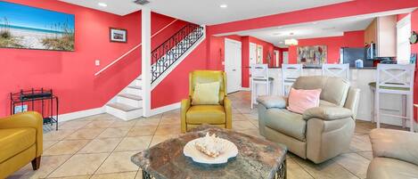 A spacious living room with a red accent wall, a staircase, and a kitchen area visible through an open doorway.