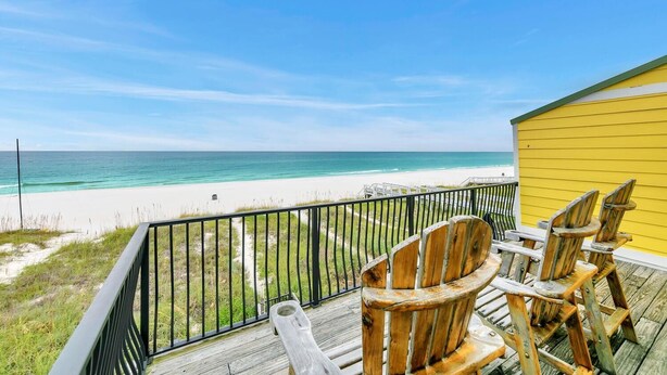Eine Holzterrasse mit Stühlen mit Blick auf einen Strand.