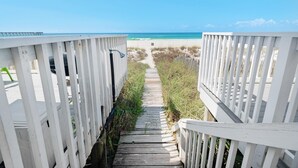 Ein hölzerner Weg führt zu einem Strand, gesäumt von weißen Geländern.