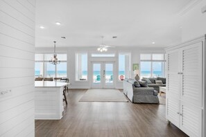 A spacious living area with a view of the beach, a dining area, and a kitchen with white cabinetry. - Fishers (Panama City Beach)