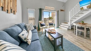 A modern living room with a grey sofa, a coffee table, and a staircase leading to an upper level. - Endless Summer F9 (Panama City Beach)