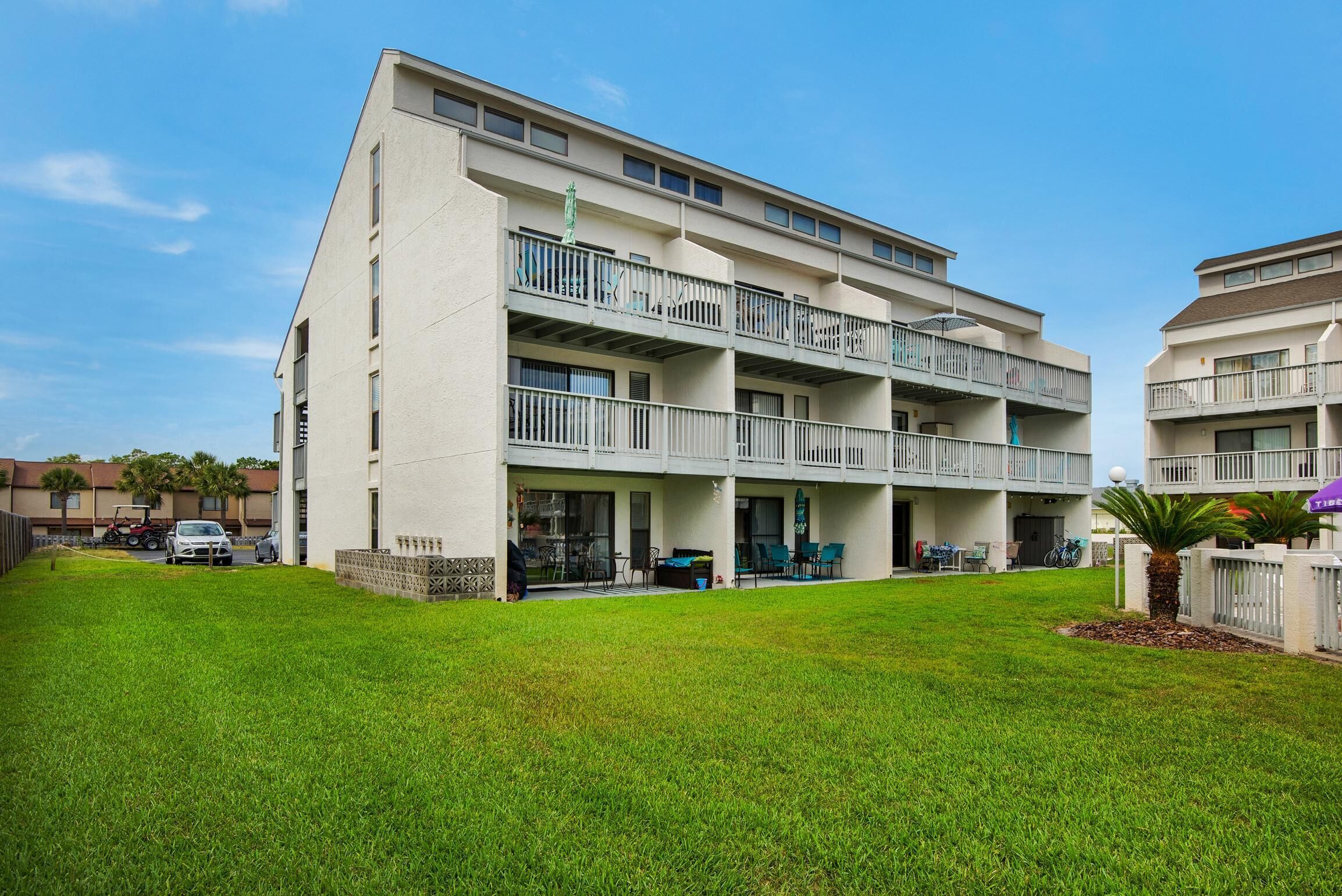 A multi-story residential building with balconies, a grassy lawn, and a clear blue sky.