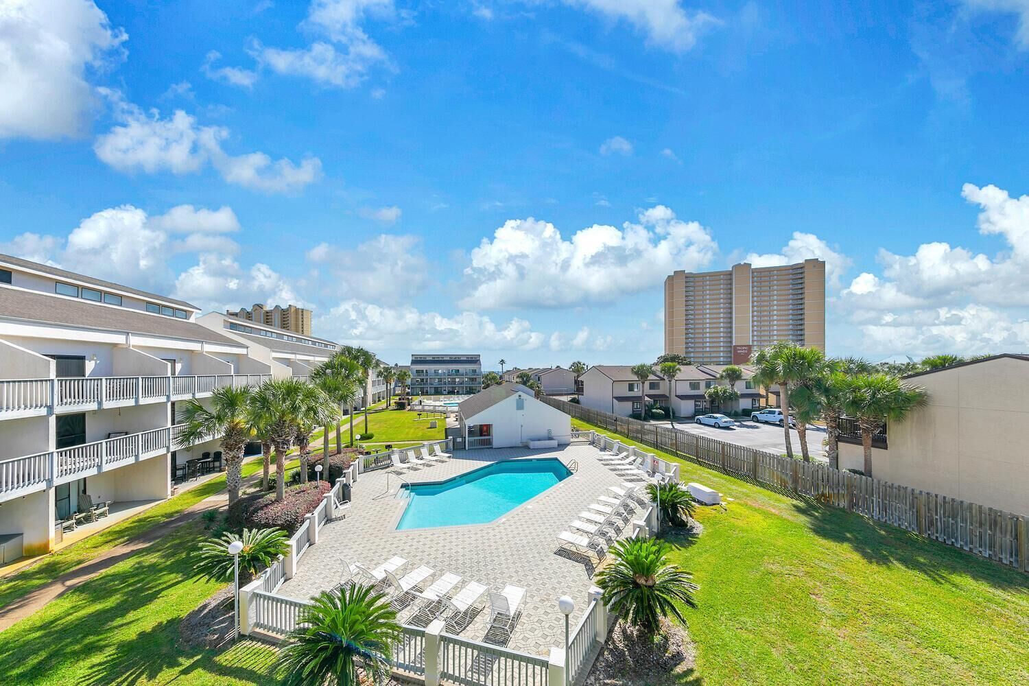 A hotel with a swimming pool, multiple balconies, and a view of a tall building in the background.