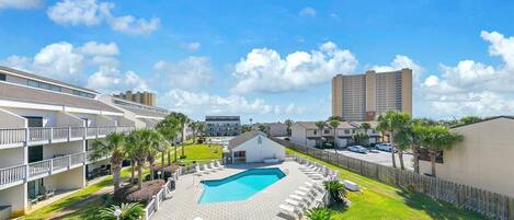 A hotel with a swimming pool, multiple balconies, and a view of a tall building in the background.