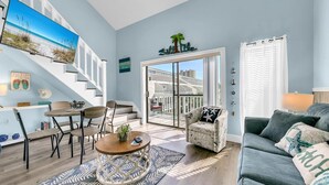 A living room with a large TV, a dining area, a sofa, and a view of the outside. - Endless Summer F11 (Panama City Beach)
