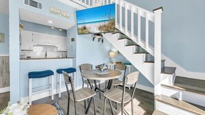 A modern kitchen with white cabinets, a dining area with a round table and chairs, and a staircase with a view of the beach. - Endless Summer F11 (Panama City Beach)