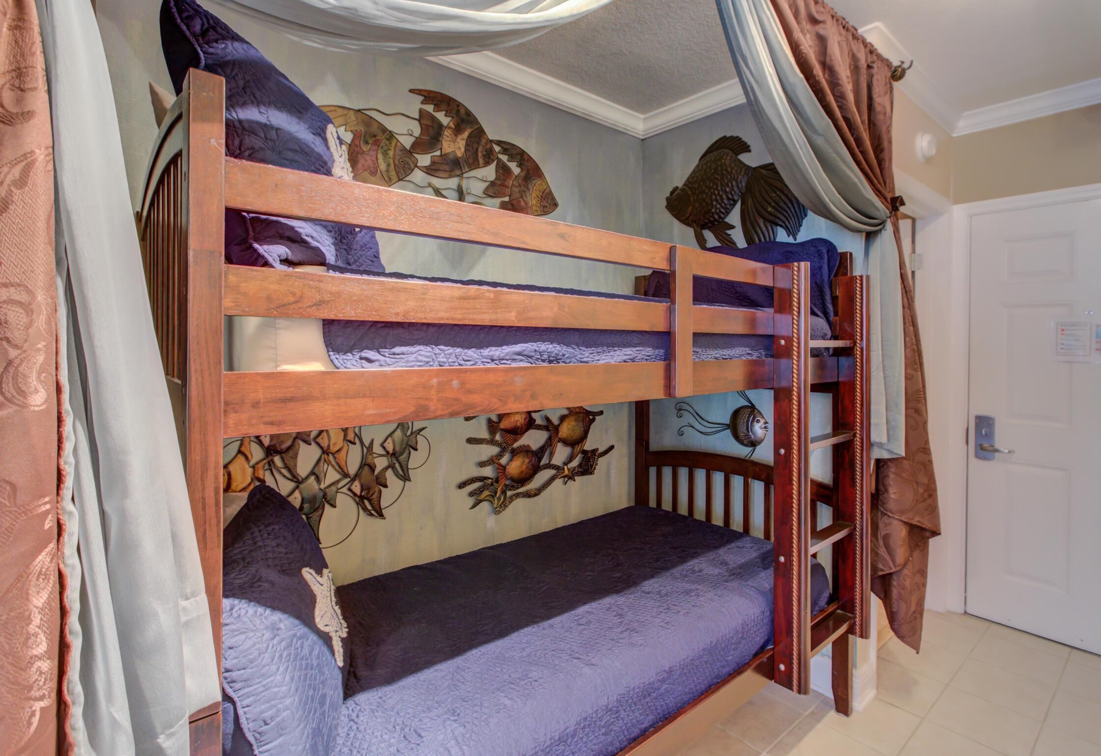 Un letto a castello con una scala, una parete decorata con illustrazioni di pesci e uccelli, e una porta con un interruttore della luce.