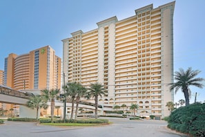 A high-rise hotel with multiple balconies, a covered walkway, and palm trees.