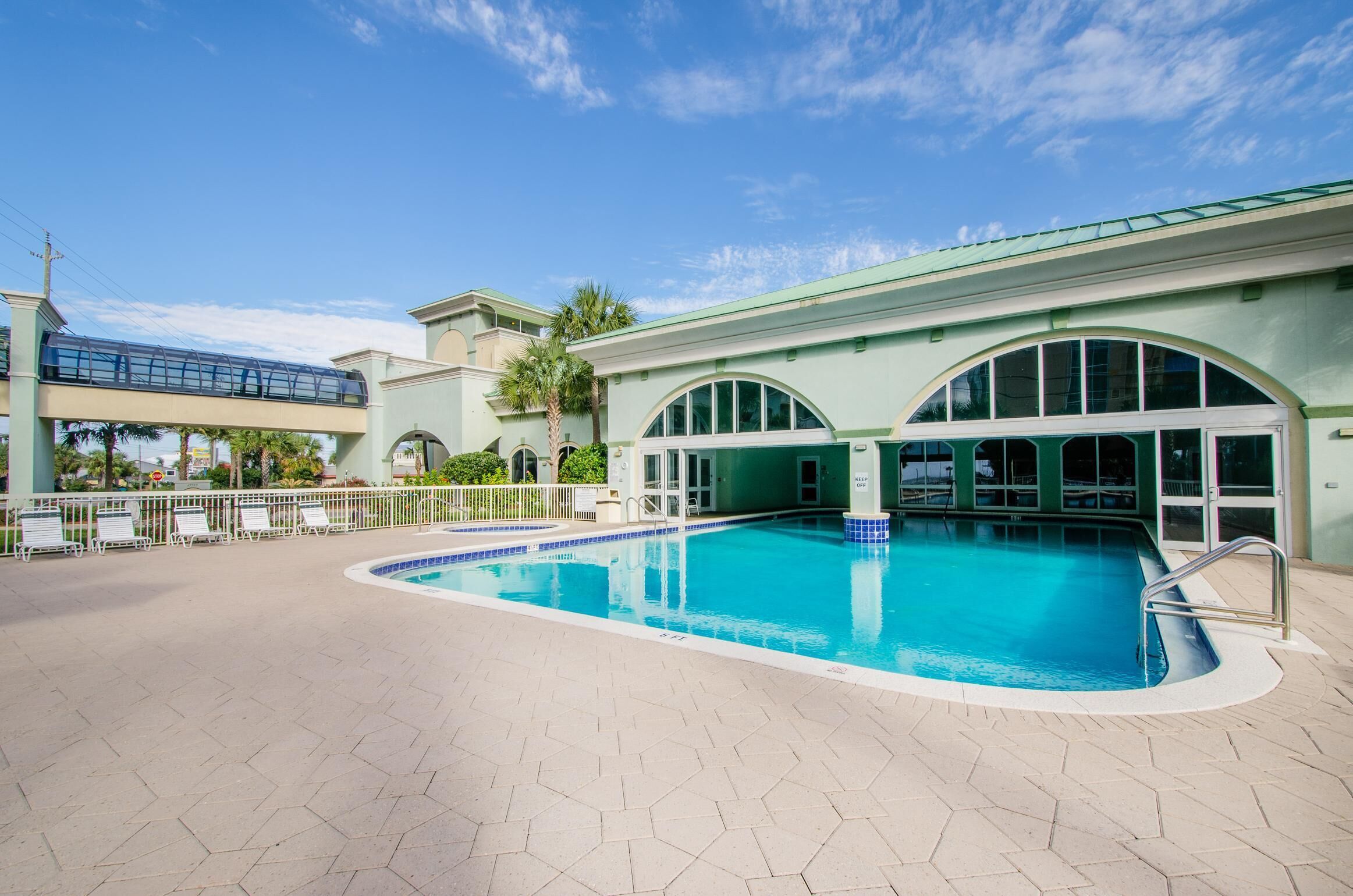 A swimming pool with a tiled deck, a covered area with a glass roof, and a palm tree in the background.