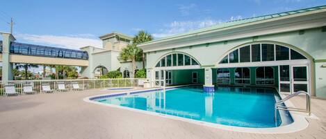A swimming pool with a tiled deck, a covered area with a glass roof, and a palm tree in the background.
