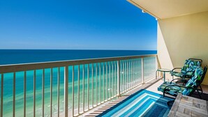 A balcony with a view of the ocean, a wooden railing, and two chairs with a blue and white striped rug. - Celadon 1902 "aloha No Ka Oi" (Panama City Beach)