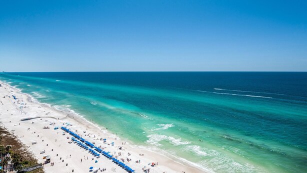 A beach with a row of blue umbrellas and a sandy shoreline. - Celadon 1902 "aloha No Ka Oi" (Panama City Beach)