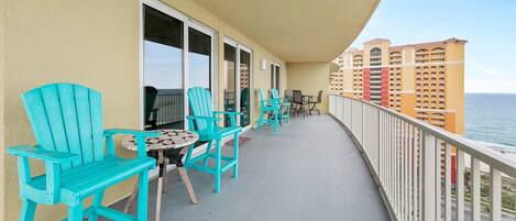 A balcony with turquoise chairs and a small table, overlooking a body of water and a hotel building.
