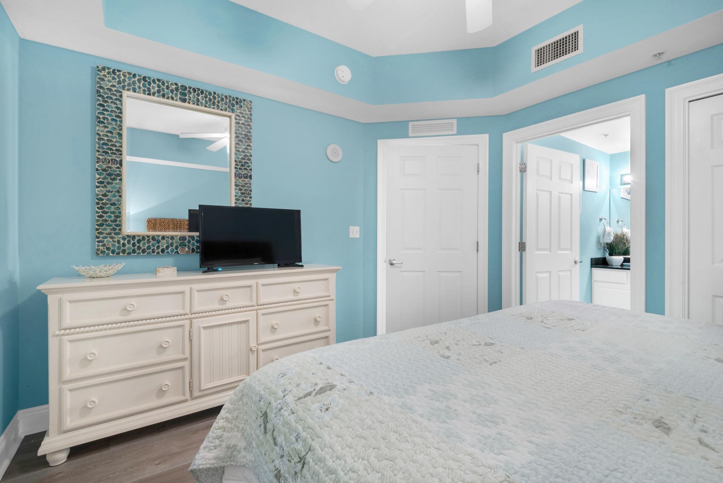 A bedroom with a bed, a dresser, a television, and a mirror.