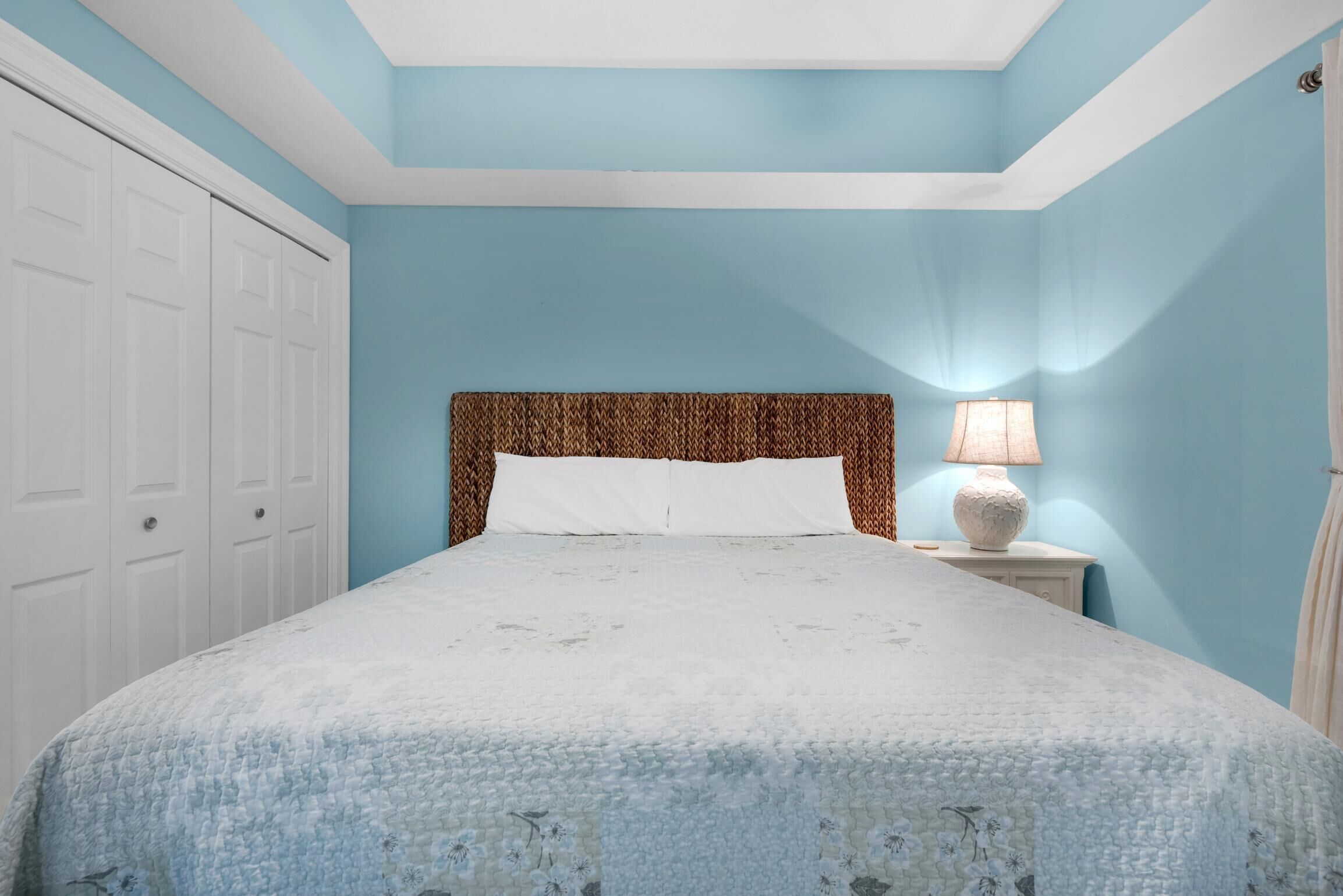 A bedroom with a bed, white nightstands, a lamp, and a wardrobe.