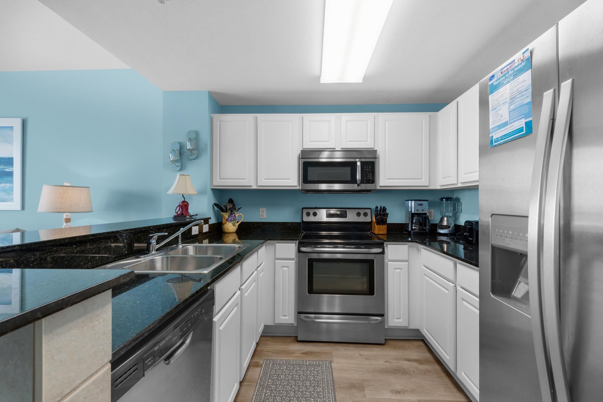 Une cuisine moderne avec des meubles blancs, des appareils en acier inoxydable, un plan de travail noir et un mur bleu.