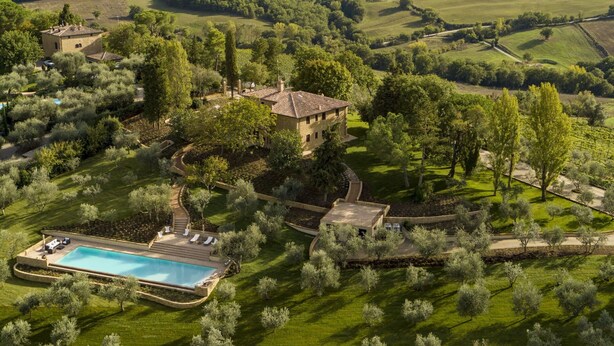 An aerial view of a countryside property with a swimming pool, a stone house, and surrounding greenery.