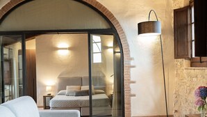 Ein modernes Schlafzimmer mit großem, bogenförmigen Durchgang zum Badezimmer, einem Sofa, einem Nachttisch mit einem Buch und einer Stehlampe.