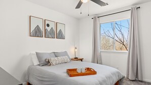 A neatly arranged bedroom with a bed, a bedside table, a tray with two cups, and a window with curtains. - Casa Blanca  (Kyle)