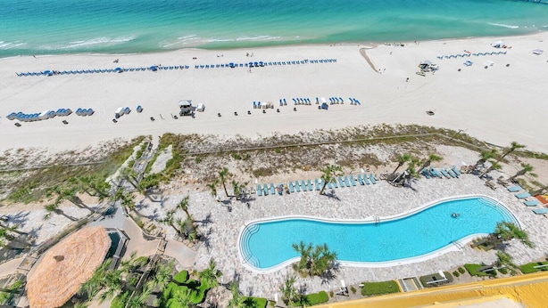 An aerial view of a beach resort with a swimming pool, beach umbrellas, and a pier.