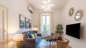 Een moderne woonkamer met een bank, fauteuils, een salontafel, een televisie en kunst aan de muur.