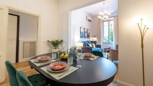 Een eetgedeelte met een ronde tafel voor vier personen, een bankstel op de achtergrond en een moderne kroonluchter.