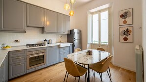 Een moderne keuken met grijze kastjes, een marmeren aanrecht en een eethoek met een ronde tafel en stoelen.