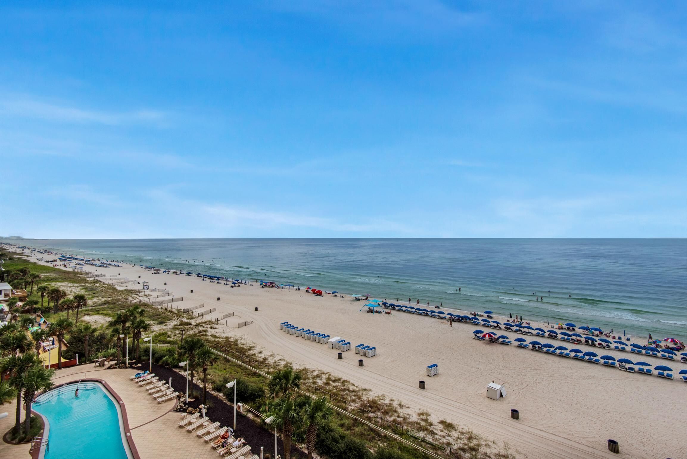 A beach resort with a swimming pool, beach umbrellas, and lounge chairs.