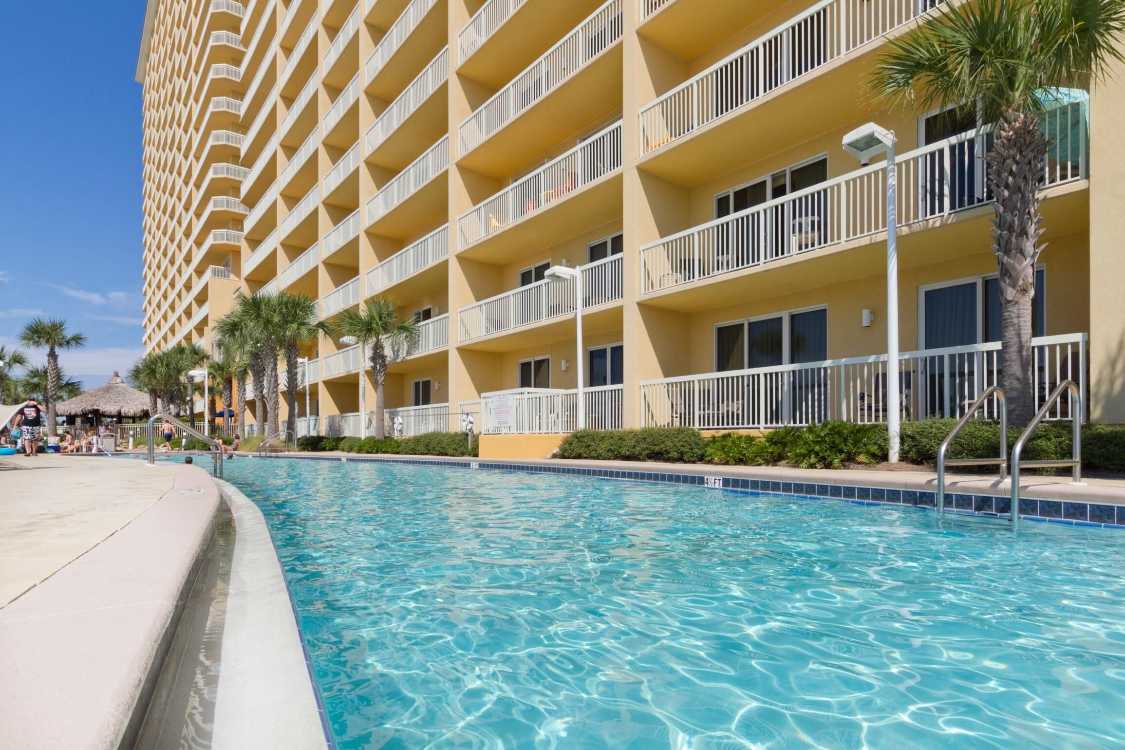A hotel with a pool, multiple balconies, and palm trees.