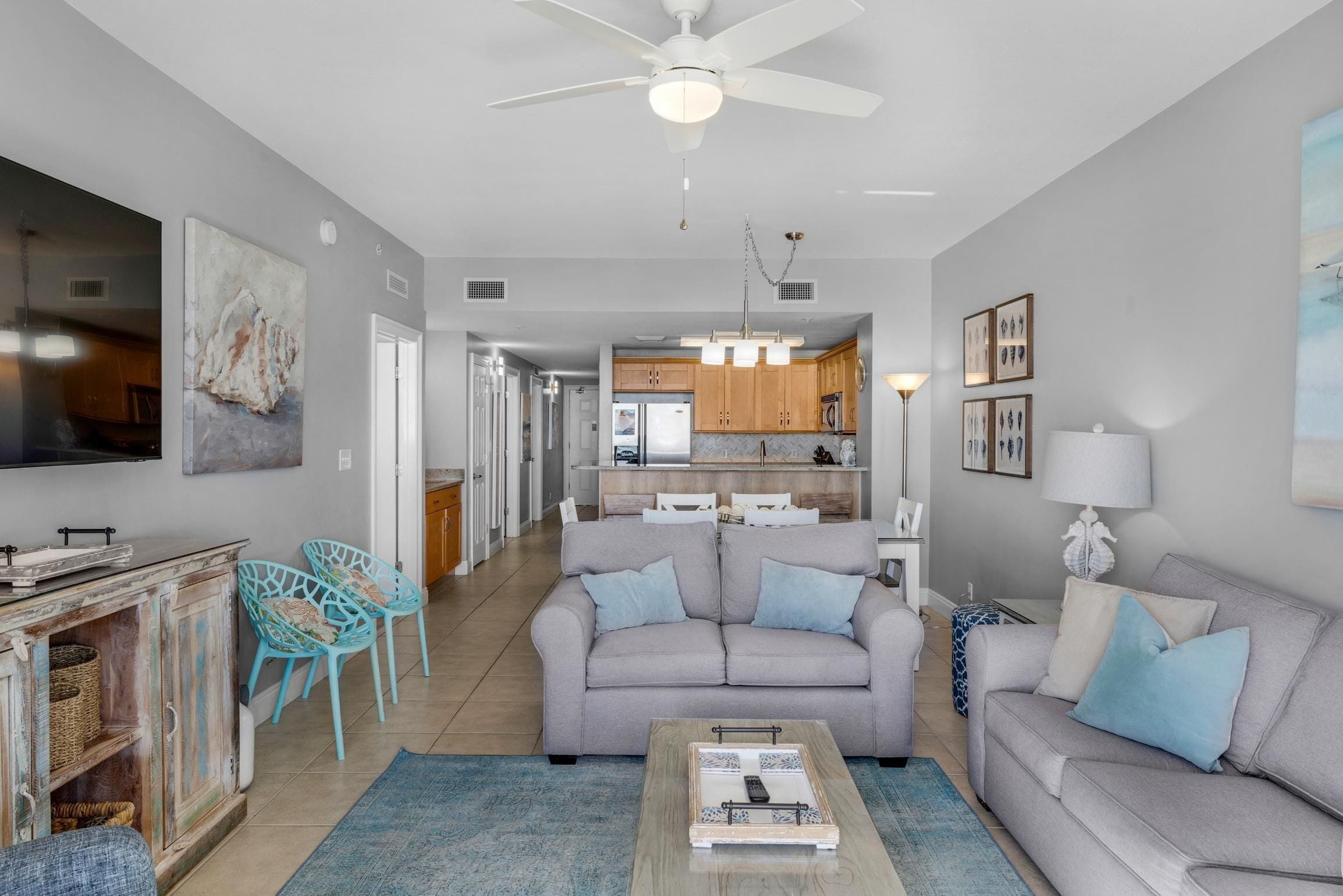 A modern living room with a grey sofa, blue chairs, a coffee table, and a kitchen in the background.