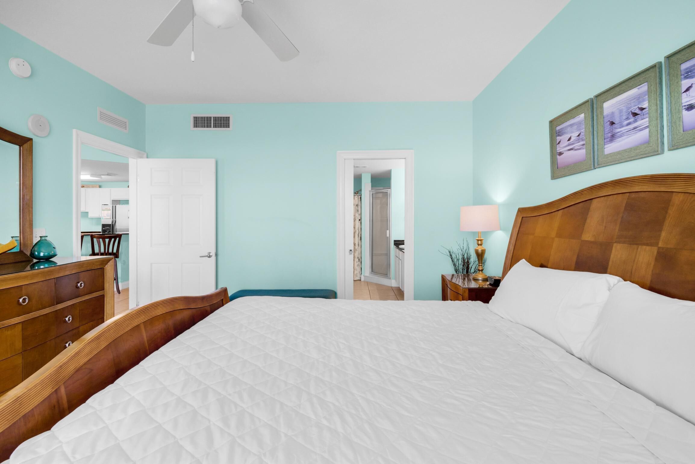 A bedroom with a large bed, wooden headboard, a dresser, a mirror, and a door leading to a bathroom.