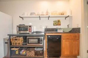 Une cuisine compacte équipée d’un four à micro-ondes, d’un grille-pain et d’un lave-vaisselle, le tout installé sur un plan de travail en bois.
