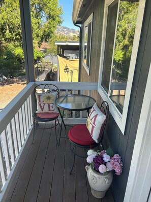 A wooden deck with two chairs and a table, a potted plant with flowers, and a view of a mountain in the background.
