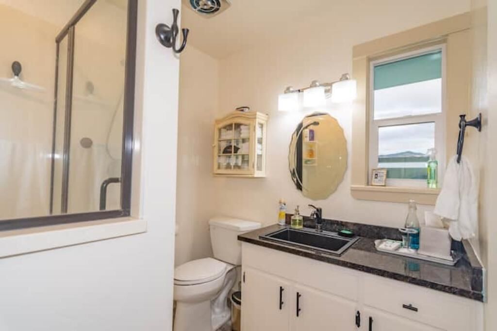 A bathroom with a toilet, sink, and shower. There is a cabinet with glass doors and a mirror above the sink.