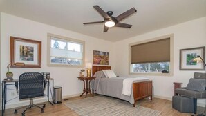 Une chambre à coucher comprenant un lit, un bureau, une chaise, un ventilateur de plafond et de grandes fenêtres.