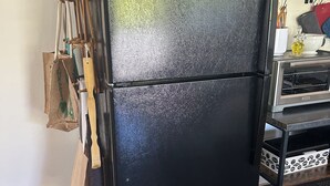 Ett svart kylskåp med en flätad korg ovanpå, ett träställ för köksredskap till vänster och en liten ugn med toastfunktion till höger.