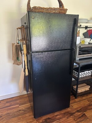 Un réfrigérateur noir sur lequel est posé un panier tressé, un porte-ustensiles en bois sur la gauche et un four grille-pain sur la droite.