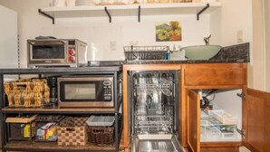 Une cuisine compacte dotée d’un four encastré, d’un four à micro-ondes et d’un lave-vaisselle, ainsi que d’une étagère au-dessus pour ranger divers ustensiles de cuisine.