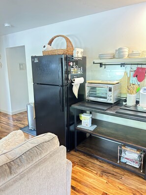Une cuisine compacte avec un réfrigérateur noir, un grille-pain et un petit plan de travail sur lequel sont disposés divers objets.
