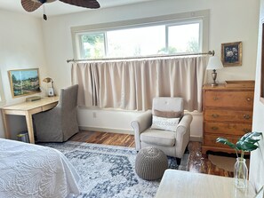 Une pièce comprenant un bureau, une chaise, une table de chevet et une fenêtre avec des rideaux.