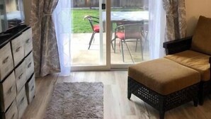 En stue med sofa, TV og en skydedør, der fører ud til en terrasse med udendørs møbler.