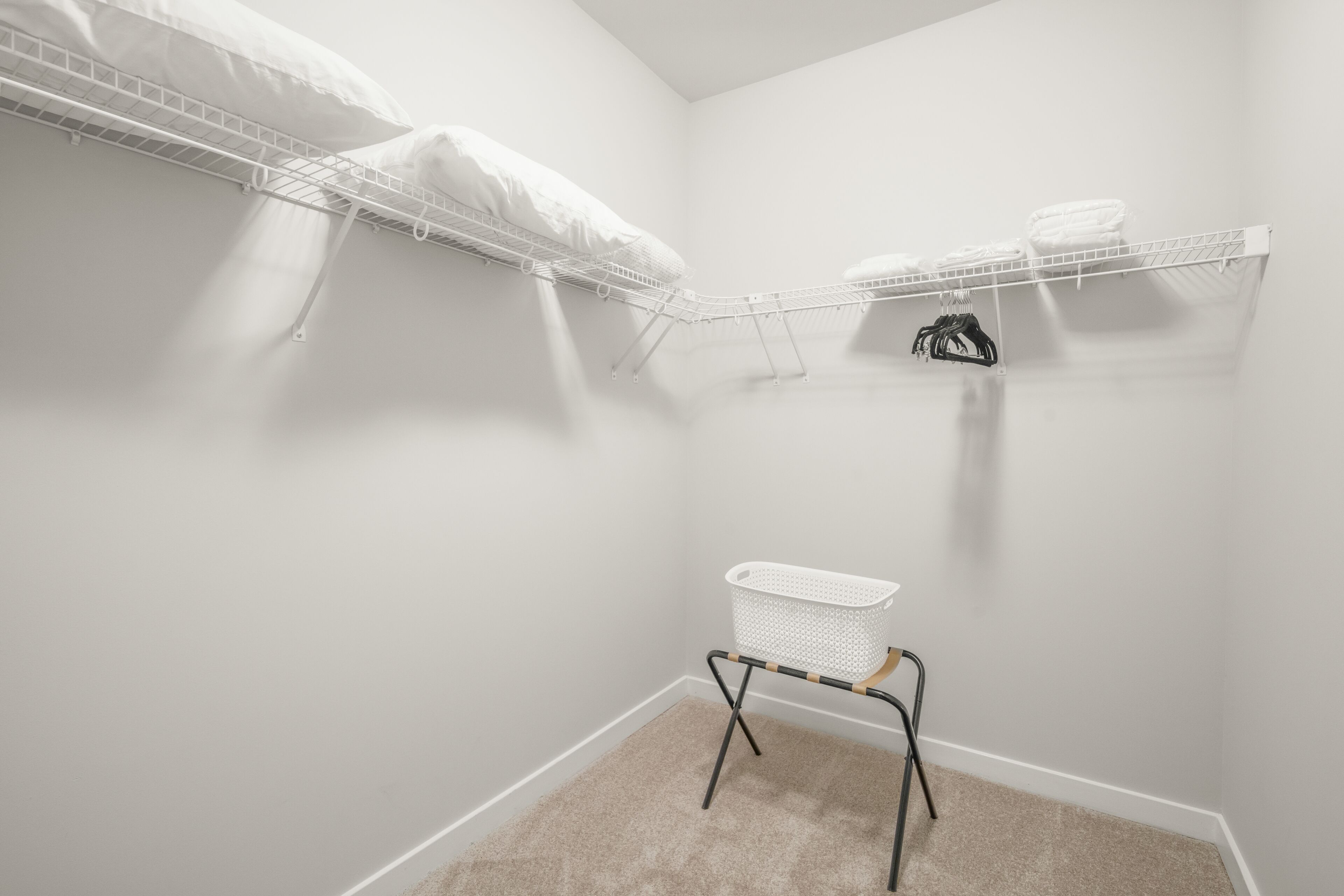 A small laundry room with a white wire shelf holding folded towels and a white laundry basket on a metal stand.
